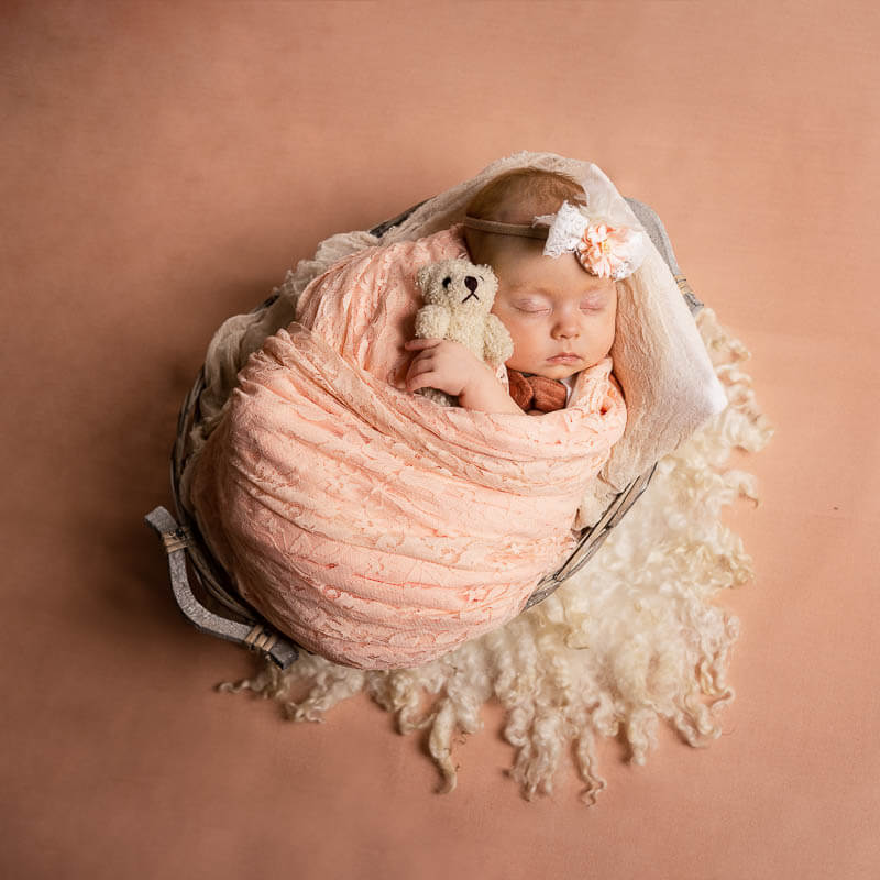 sleeping newborn baby in a basket against pink background